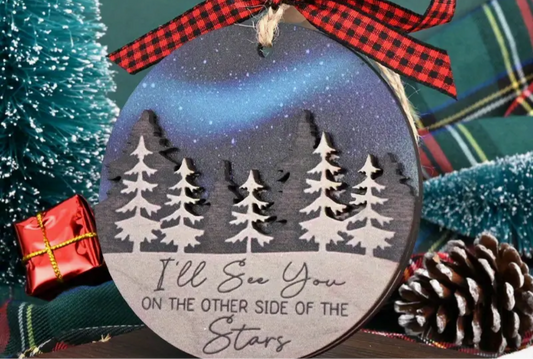 a christmas tree ornament in front of a blurred red 'holiday lights' background. This ornament can be customized with a name, honoring the memory of those who are not with us during the holiday season. "I'll see you on the other side of the stars"