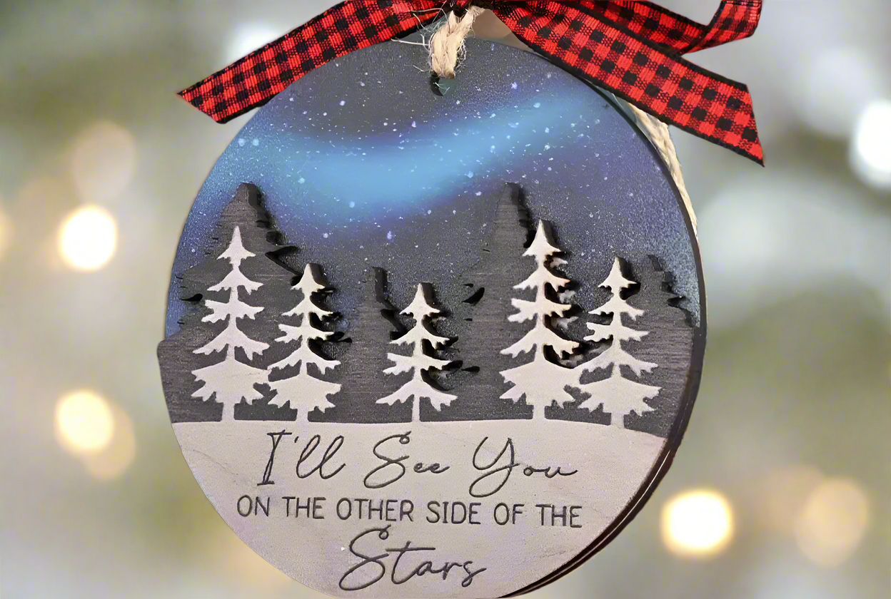 a Christmas tree ornament in front of a blurred golden  'holiday lights' background. This ornament can be customized with a name, honoring the memory of those who are not with us during the holiday season. "I'll see you on the other side of the stars"