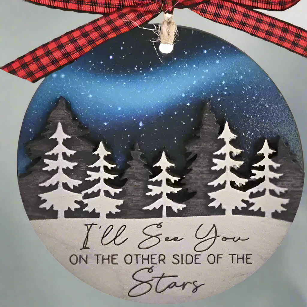 a christmas tree ornament in front of a blurred red 'holiday lights' background. This ornament can be customized with a name, honoring the memory of those who are not with us during the holiday season. "I'll see you on the other side of the stars"